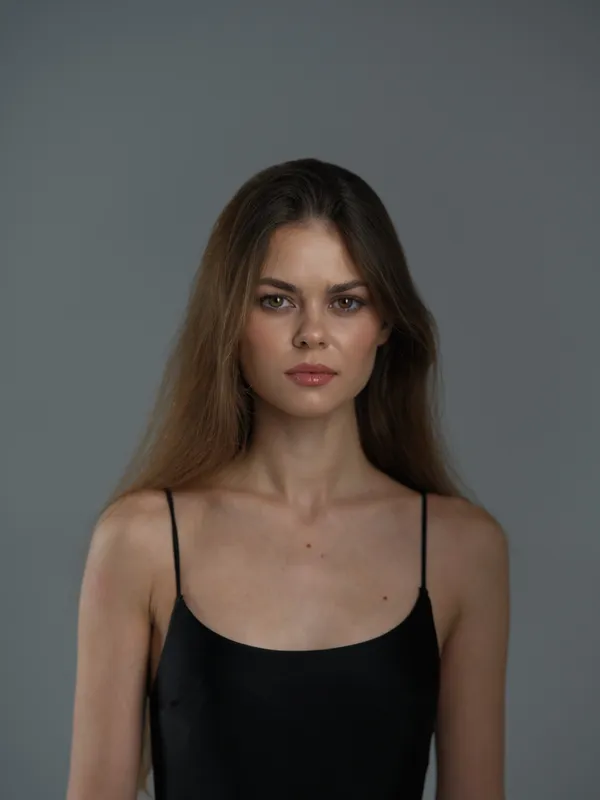 young woman with serious expression wearing black top against grey background
