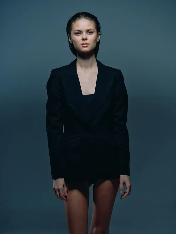 young woman in black blazer standing confidently with serious expression in dark studio background