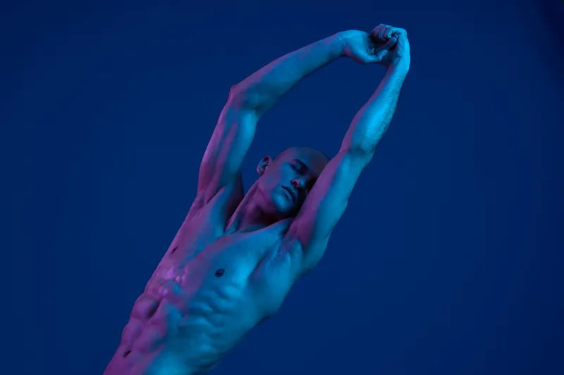Athletic man stretching under soft blue light, conveying a sense of relaxation and wellness. A dynamic pose highlights strength and fluidity in a serene atmosphere.
