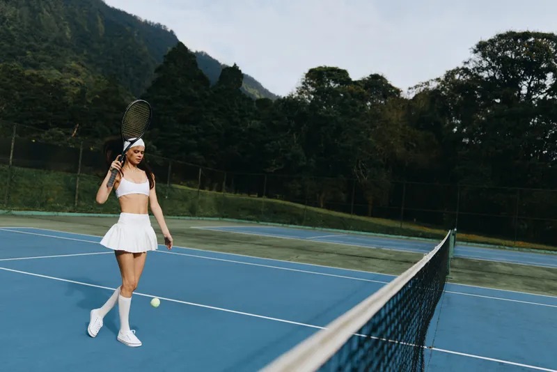 Female tennis player in white sportswear on blue court, captured during motion with a tennis racket, showcasing determination and athleticism in a natural setting