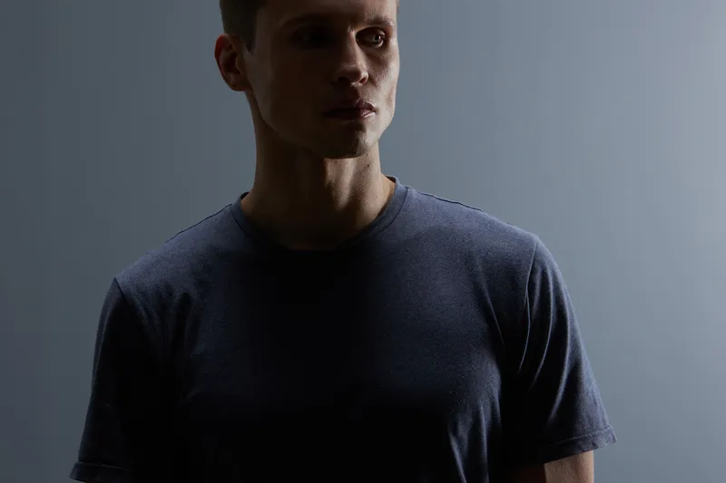 Dark silhouette of young man with short hair in plain casual t-shirt, minimal background, moody lighting creating a mysterious atmosphere, indoors studio shot. People portrait concept