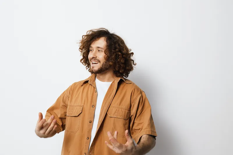 Smiling man with curly hair in a brown shirt, expressing joy against a light background, ideal for concepts of happiness and lifestyle