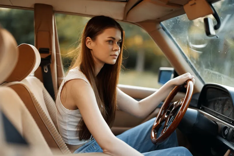 Young woman driving a vintage car, showcasing serene emotions and natural beauty in a sunlit outdoor setting, emphasizing freedom and adventure.