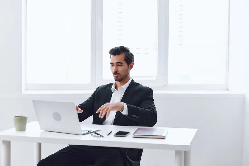Мужчина в костюме сидит за компьютером в офисе, выглядит уставшим и задумчивым, испытывая разочарование