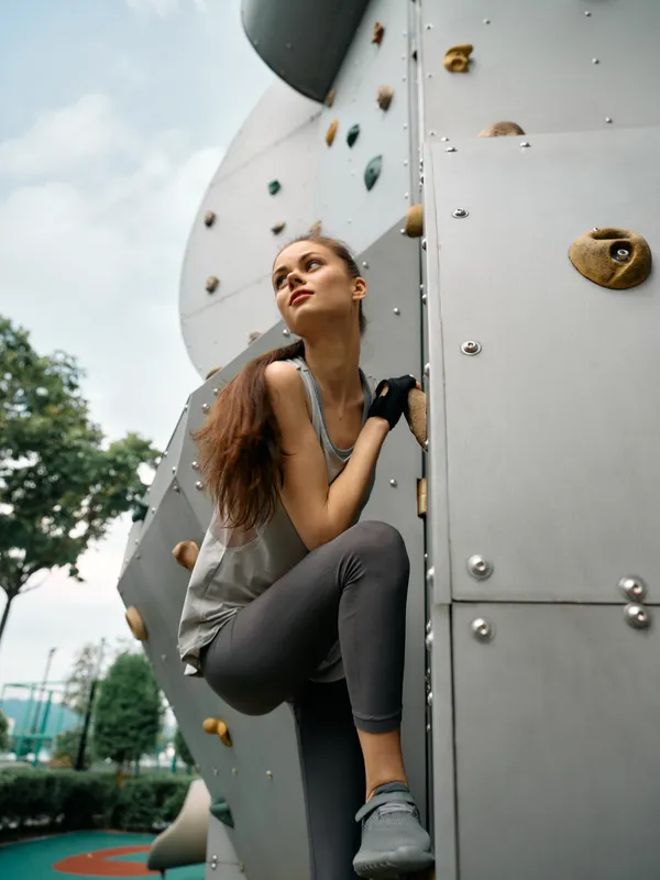 Спортивная девушка-скалолаз в фитнес-одежде поднимается по скалодрому в парке