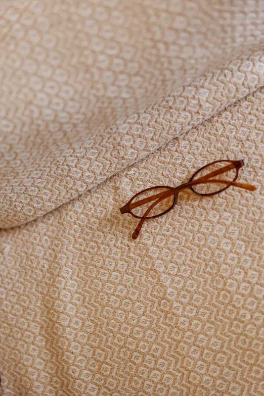Closeup of a patterned beige fabric with a pair of glasses resting on it, conveying a calm home mood and a simple lifestyle moment at home