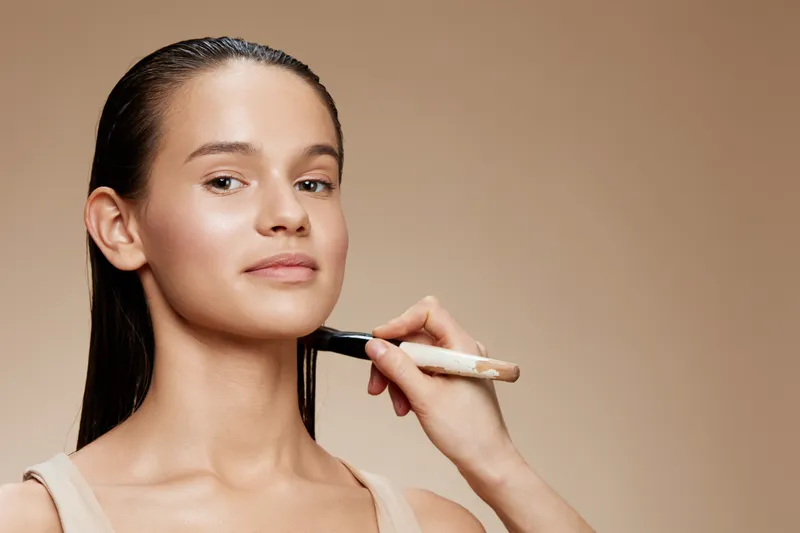 Young woman receiving makeup application with soft natural tones, showcasing beauty and confidence in a neutral setting