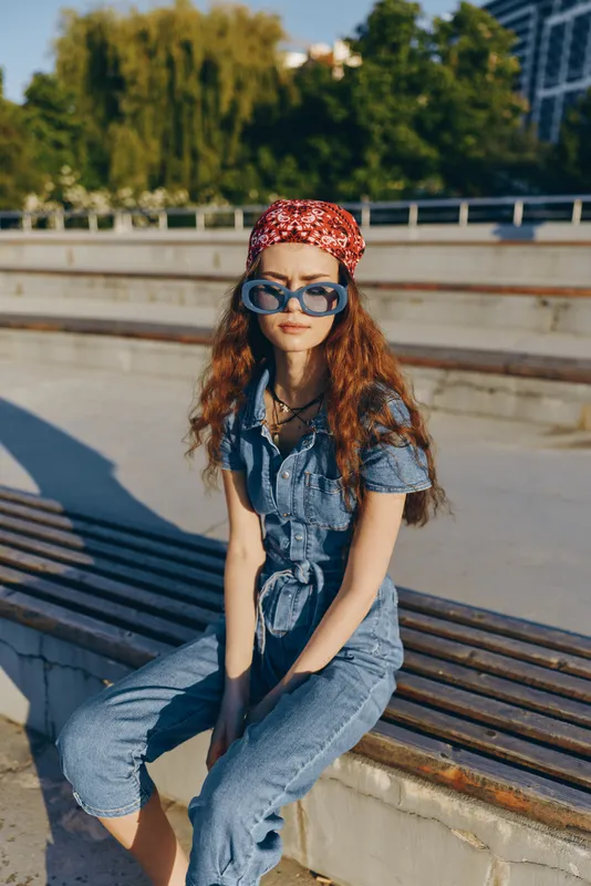 Lifestyle woman wearing modern boho-western denim street style with a red bandana and sunglasses, captured in warm film color tones during sunny outdoor moments.