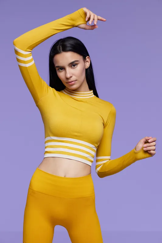 Woman sport fitness posing in yellow activewear, showing toned body and graceful stretch on purple background with focused expression and sleek black hair.