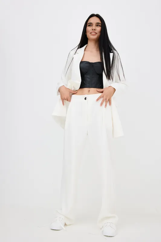 young woman wearing stylish white suit and black corset top stands confidently against white background, showcasing modern fashion and casual elegance
