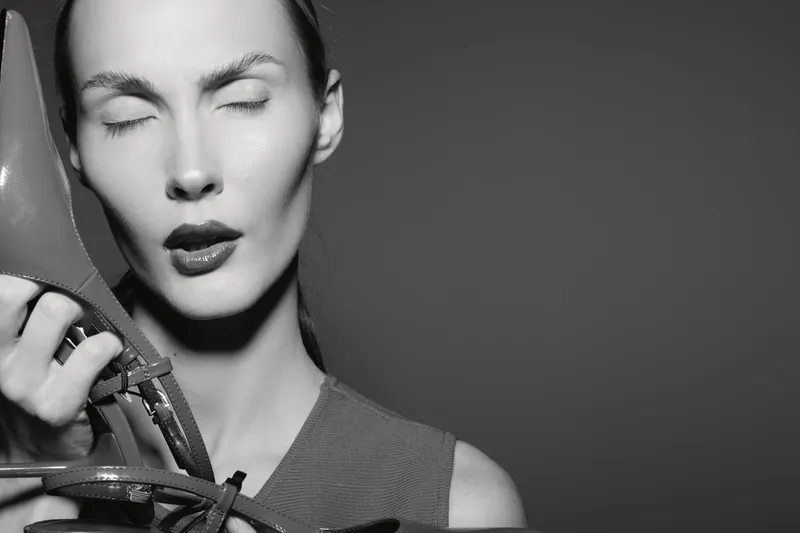 Portrait of a fair skinned Caucasian woman with closed eyes holding high heel shoes near her face in black and white studio concept.