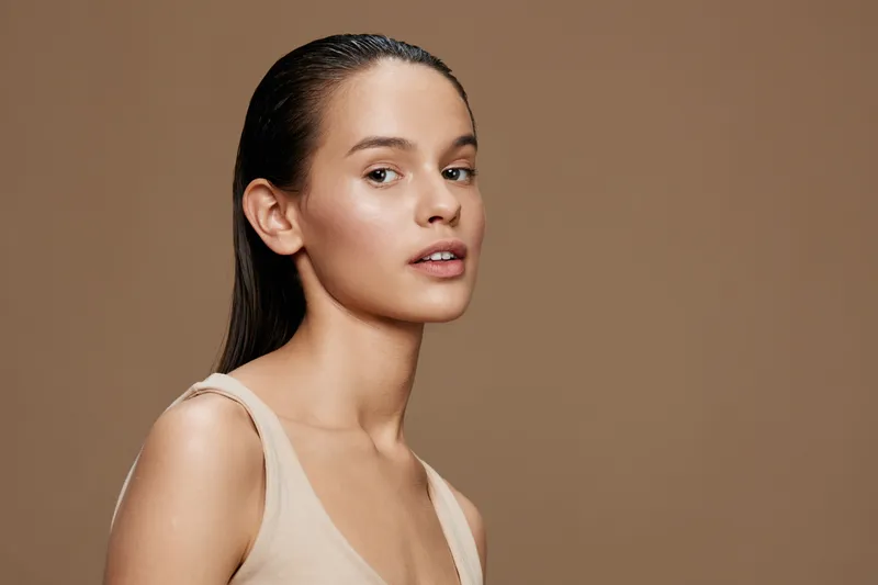 Natural beauty portrait of a young model with wet hair and smooth skin against a warm brown background, showcasing healthy and radiant skin