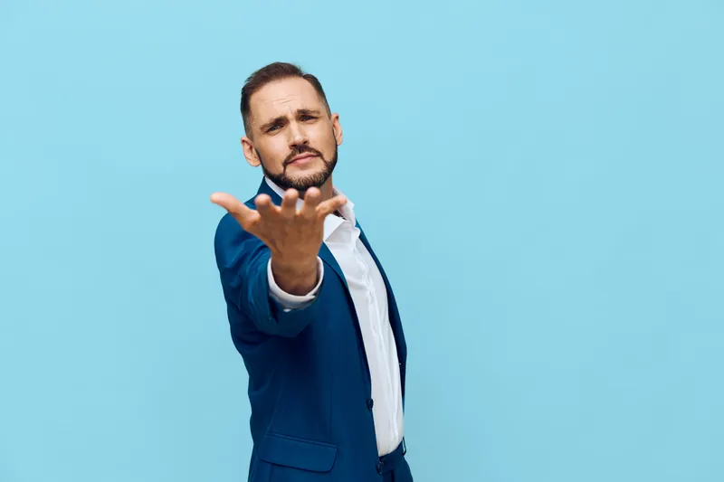 A professional man in a blue suit stands against a solid colored background, projecting confidence and focus, with an inviting open hand gesture that suggests guidance and readiness.