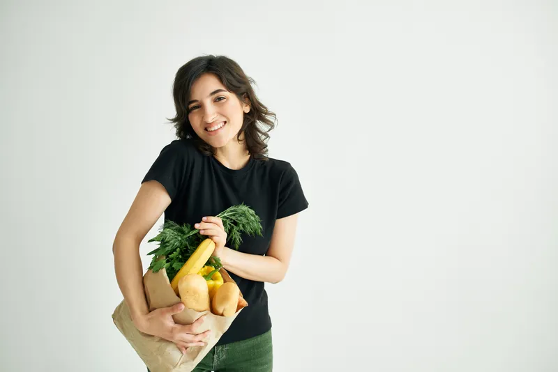 Весёлая женщина с пакетом продуктов совершает покупки
