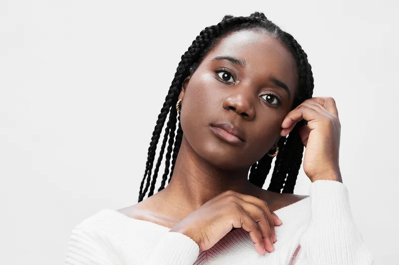 Portrait of a young female model with braided hair in a soft, light colored sweater, expressing calmness and self assurance against a neutral background