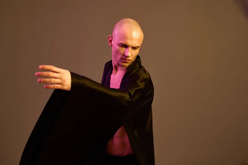 Engaging man in a flowing black robe showcases movement and grace in a captivating light setting, emphasizing his artistic expression.