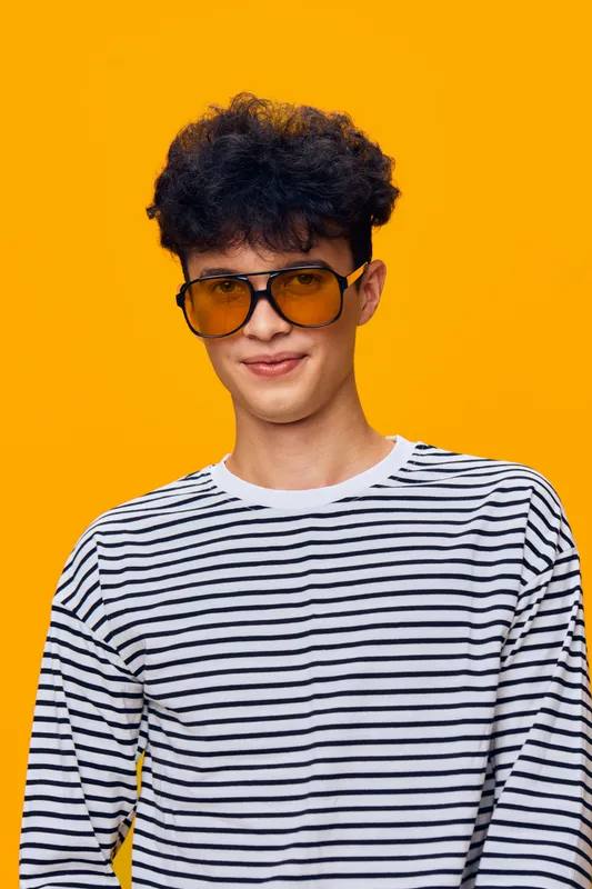 young man with sunglasses wearing a striped shirt smiling confidently against bright orange background, casual style, natural light, close-up portrait