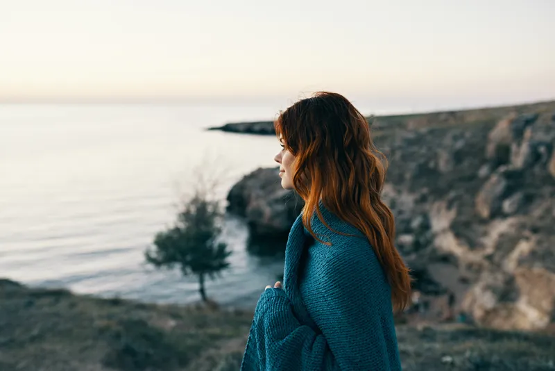 Женщина на закате у моря в горах с пледом на плечах
