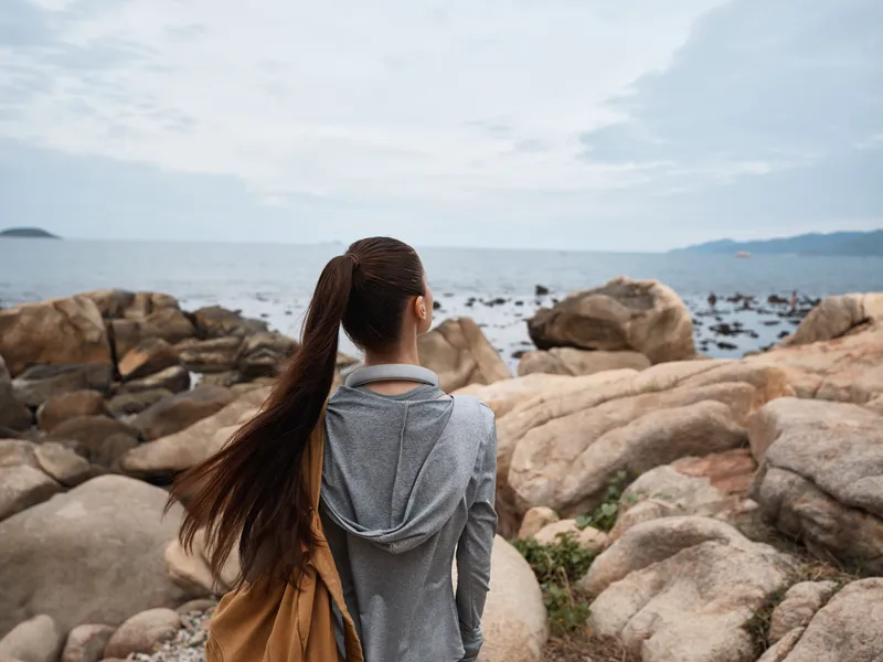 Young woman enjoying nature by the sea, wearing casual sporty attire, with long hair tied back, looking at the ocean, ideal for outdoor lifestyle and travel themes