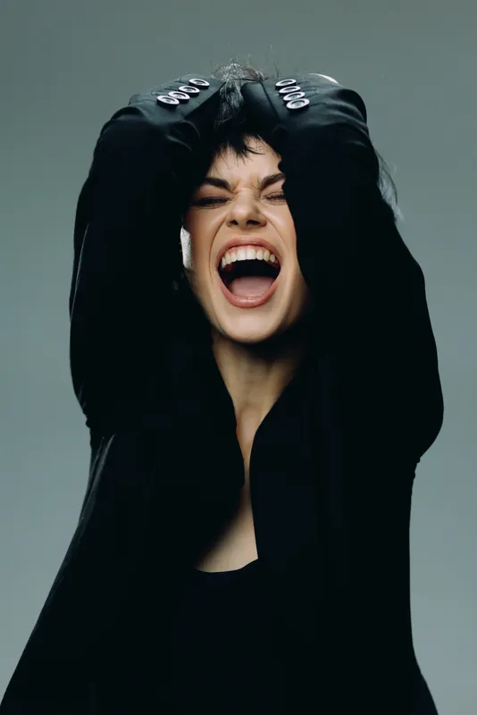 Young woman expressing intense emotion with closed eyes and open mouth in black outfit