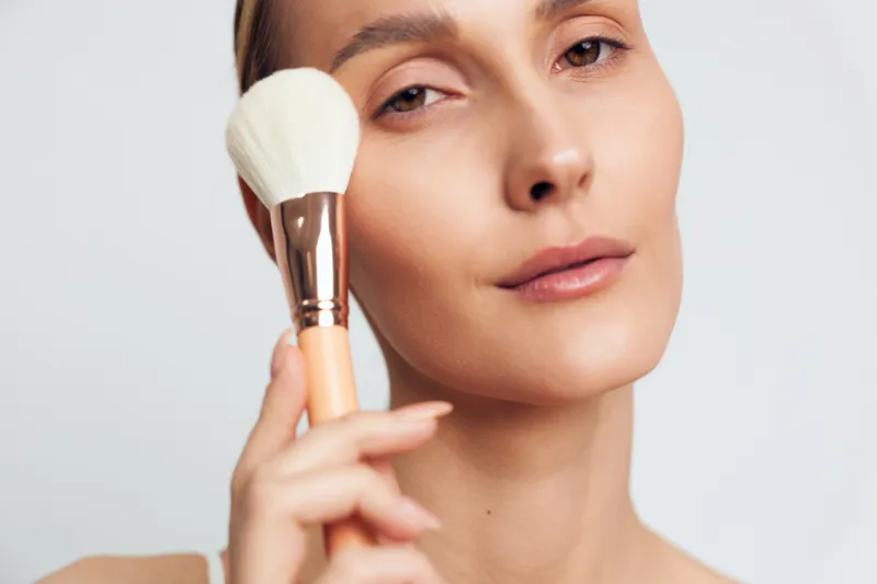 Close up of a woman applying face cream with a cosmetic brush, facial care skincare routine, beauty and wellness, self care moment with soft light on white background, calm studio portrait