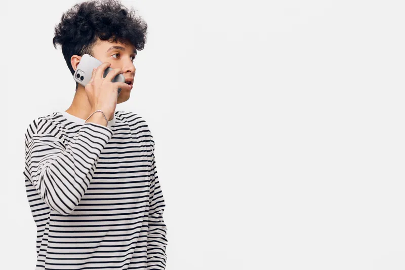 young man speaking on mobile phone wearing striped shirt, focused expression, short curly hair, casual style, isolated white background