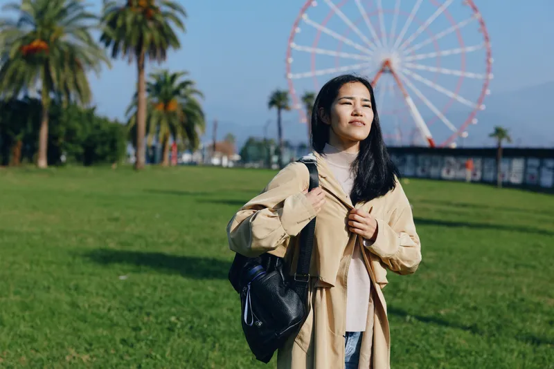 park, woman, backpack, outdoor, travel, leisure scene with casual fashion style under sunny daylight beside a ferris wheel in a spacious green park