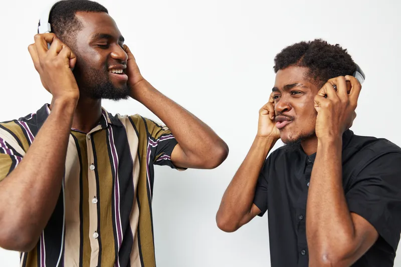 Two black men enjoying music while wearing headphones, sharing a joyful moment of connection and rhythm in a bright and modern setting.