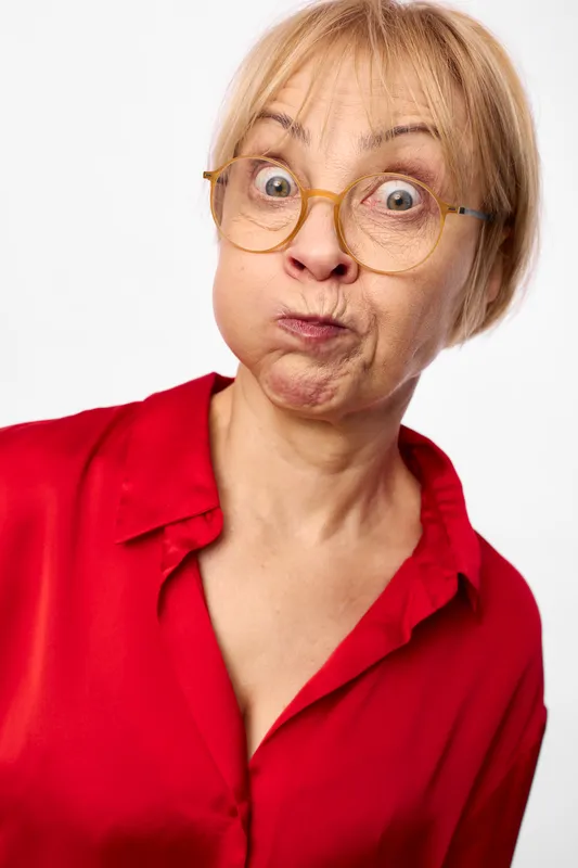 woman senior portrait surprised glasses red background expression closeup funny, studio headshot of a senior blonde woman with round glasses, shocked wide eyes and puckered lips, wrinkled skin,