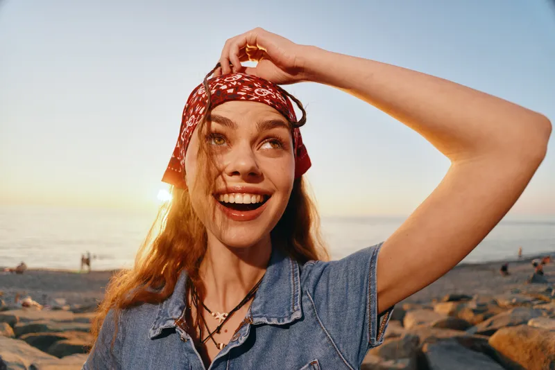 Happy woman enjoying lifestyle with modern boho-western denim street style outdoors, film color enhancing warm sunlight and joyful mood at the beach during golden hour.