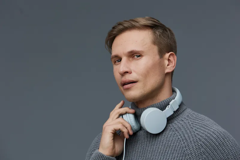 young man working with headphones wearing warm grey sweater look away thoughtful focused isolated on grey background digital nomad concept