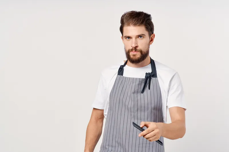 Мужчина в фартуке работает в салоне красоты, модная профессия