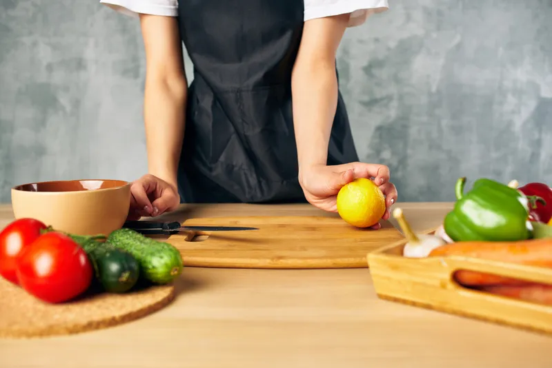 Женщина в черном фартуке на кухне нарезает овощи