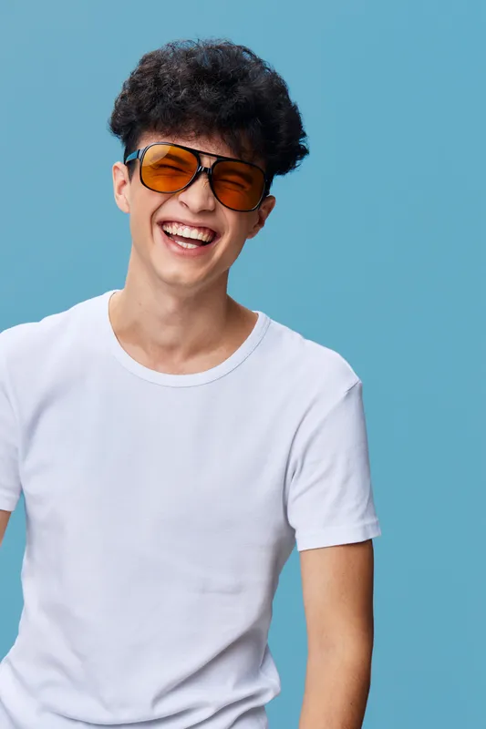 smiling man wearing orange sunglasses and a white t-shirt on blue background, curly hair, casual style, cheerful expression, youthful energy