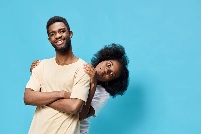 Joyful couple in casual outfits against a blue background, showcasing love and connection, with happy expressions and stylish hairstyles