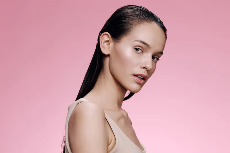Elegant young model with wet hair against a pink background, showcasing natural beauty and confidence Ideal for skincare and beauty concepts