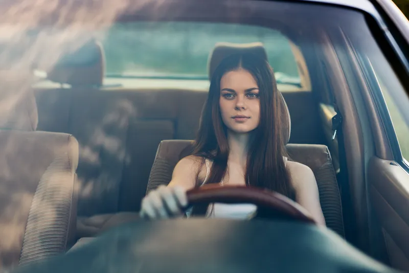 Young woman with long hair driving a car, reflecting confidence and freedom, wearing casual attire in a serene, natural setting, perfect for lifestyle concepts.