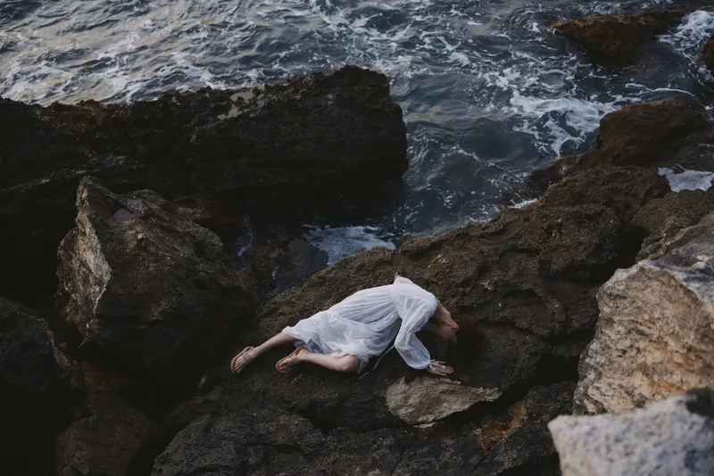 Женщина лежит на каменистом побережье с трещинами на поверхности скал