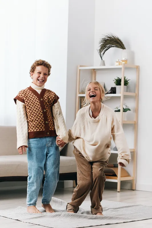Two joyful figures, a young boy and an elderly woman, hold hands and dance in a bright living room, capturing warmth, energy, and playful connection.