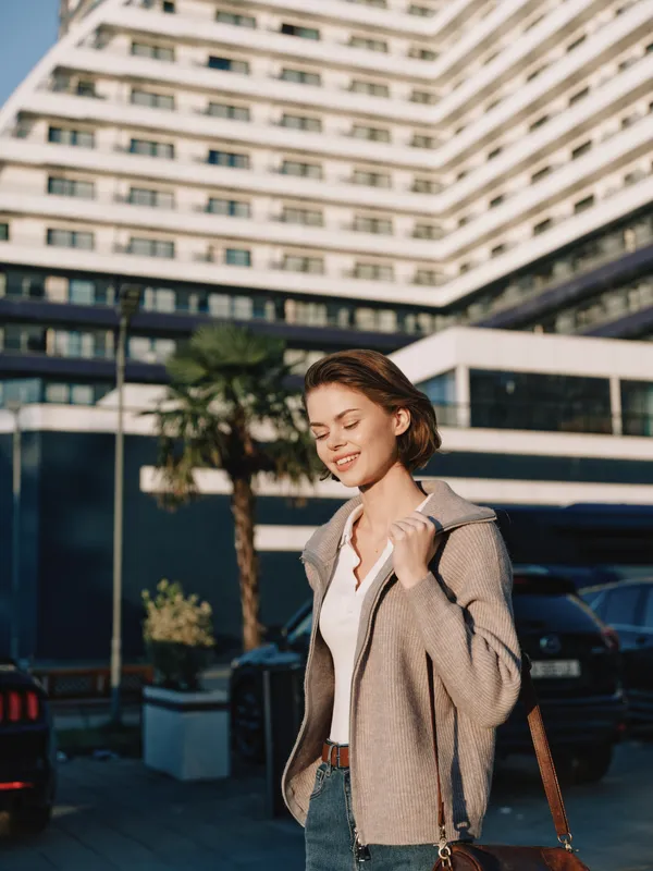 A cheerful business professional stands outside a modern office building, smiling while checking her phone. She appears confident and engaged, conveying a positive corporate atmosphere.