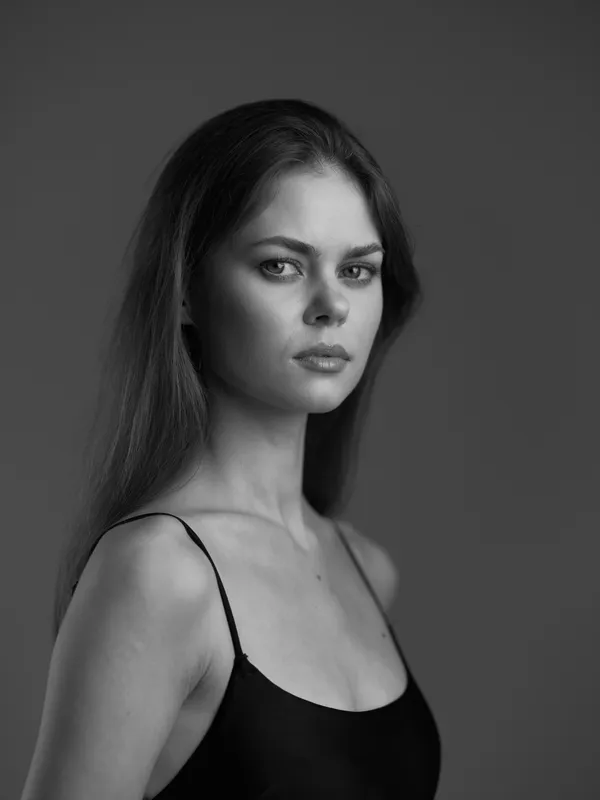 Black and white portrait of a serious woman with long hair wearing a black top against a dark background
