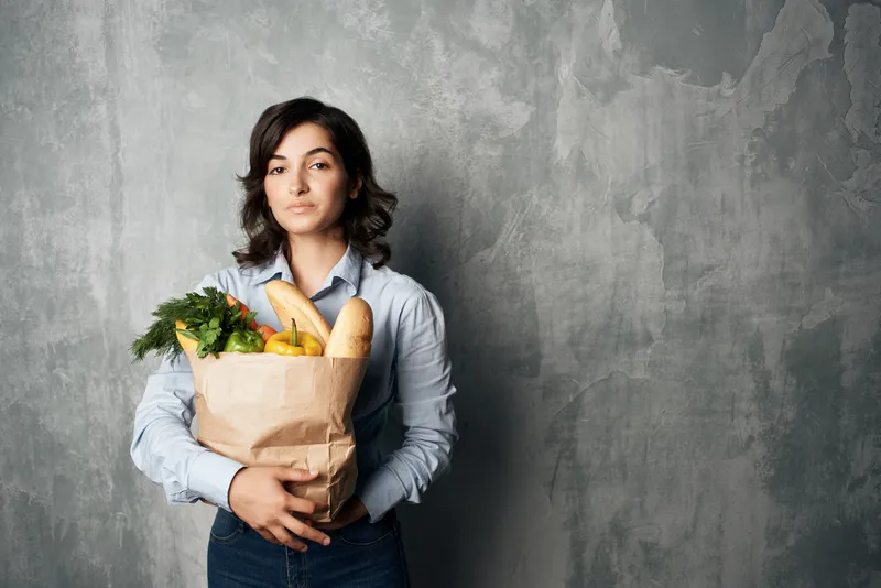 Улыбающаяся женщина с пакетом продуктов, овощами, совершающая покупки в супермаркете
