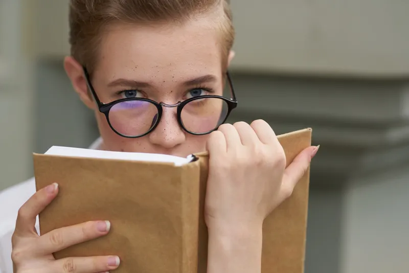 Симпатичная женщина в очках гуляет по городу с книгой, общаясь с окружающими