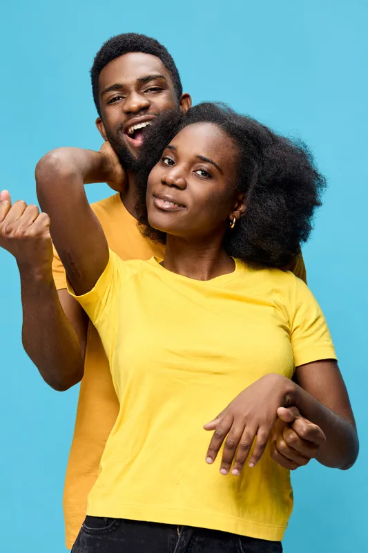 Happy young couple expressing joy with vibrant clothing against a blue background, showcasing love and connection in a playful manner