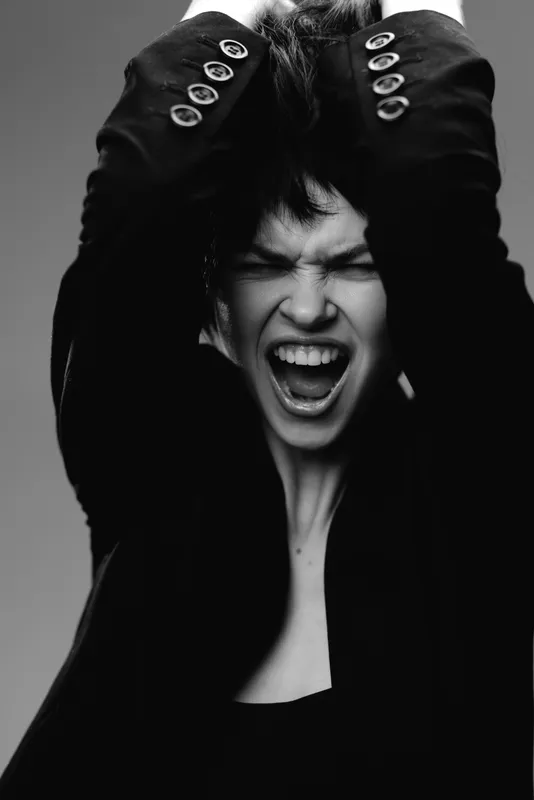 Black and white portrait of a screaming woman with hands in hair, expressing intense emotion and frustration in monochrome style.