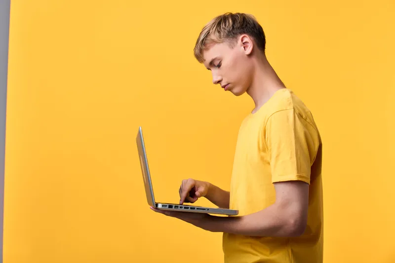 Man in a yellow t shirt using a laptop against a bright yellow background, technology focus, casual digital work, modern photography style, clean composition with minimal props.