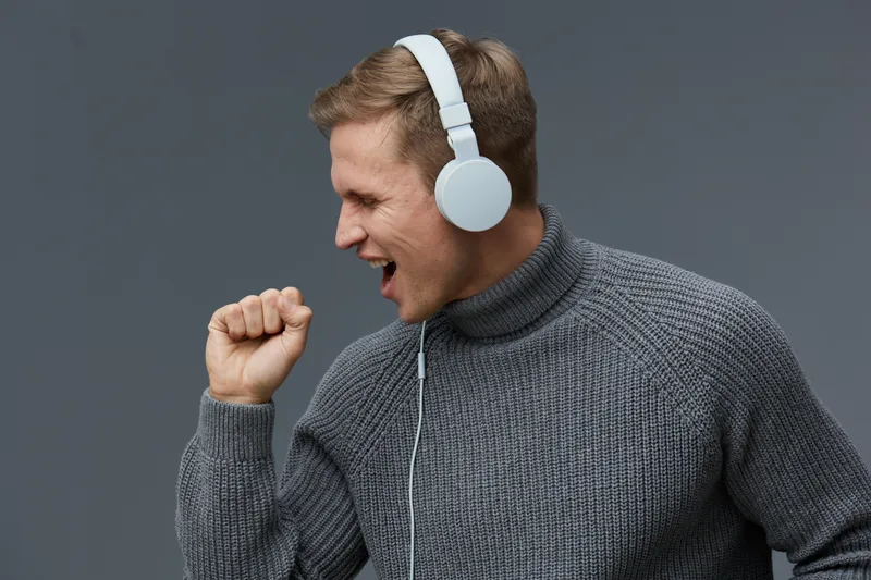 young caucasian man wearing gray sweater headphones singing enjoying music isolated on gray background digital detox concept