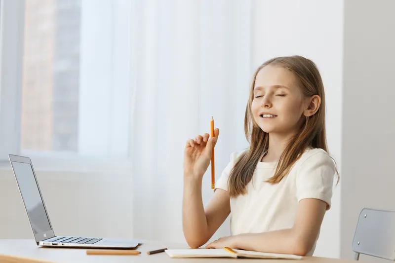 Young girl with a pen contemplating at a desk by a window, conveying creativity and focus in a bright, minimalist workspace
