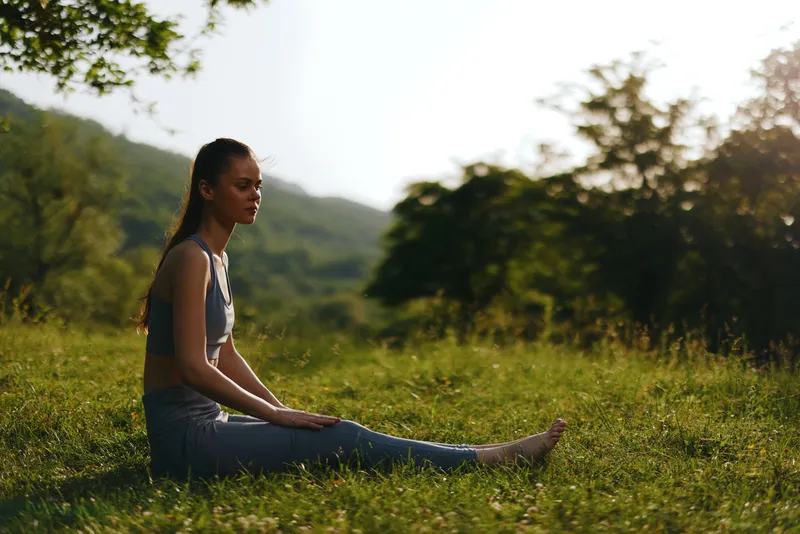 Serene young woman practicing meditation in nature, surrounded by lush greenery, capturing a peaceful moment of mindfulness in her yoga attire