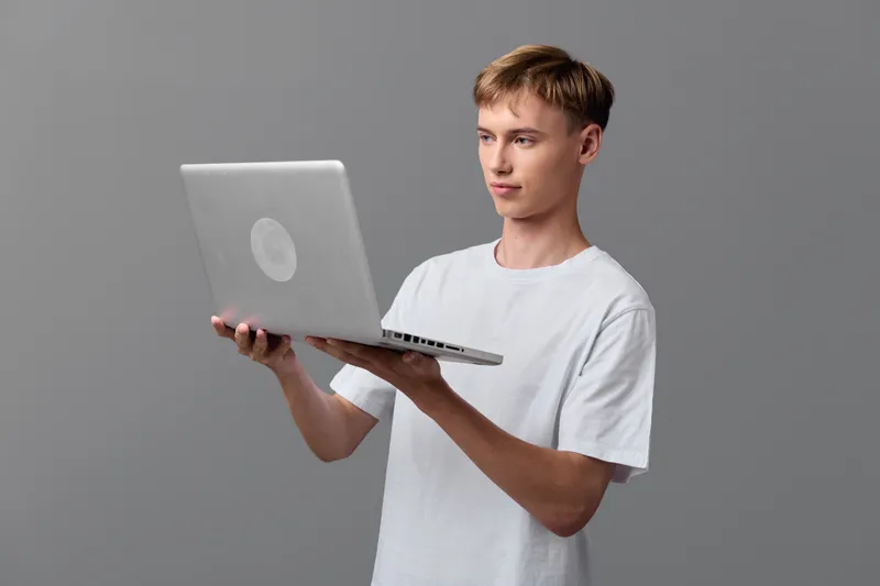 Casual man in a white tee presenting a laptop, showcasing technology and learning in a simple studio setup, focused expression, modern computing device for online work and education